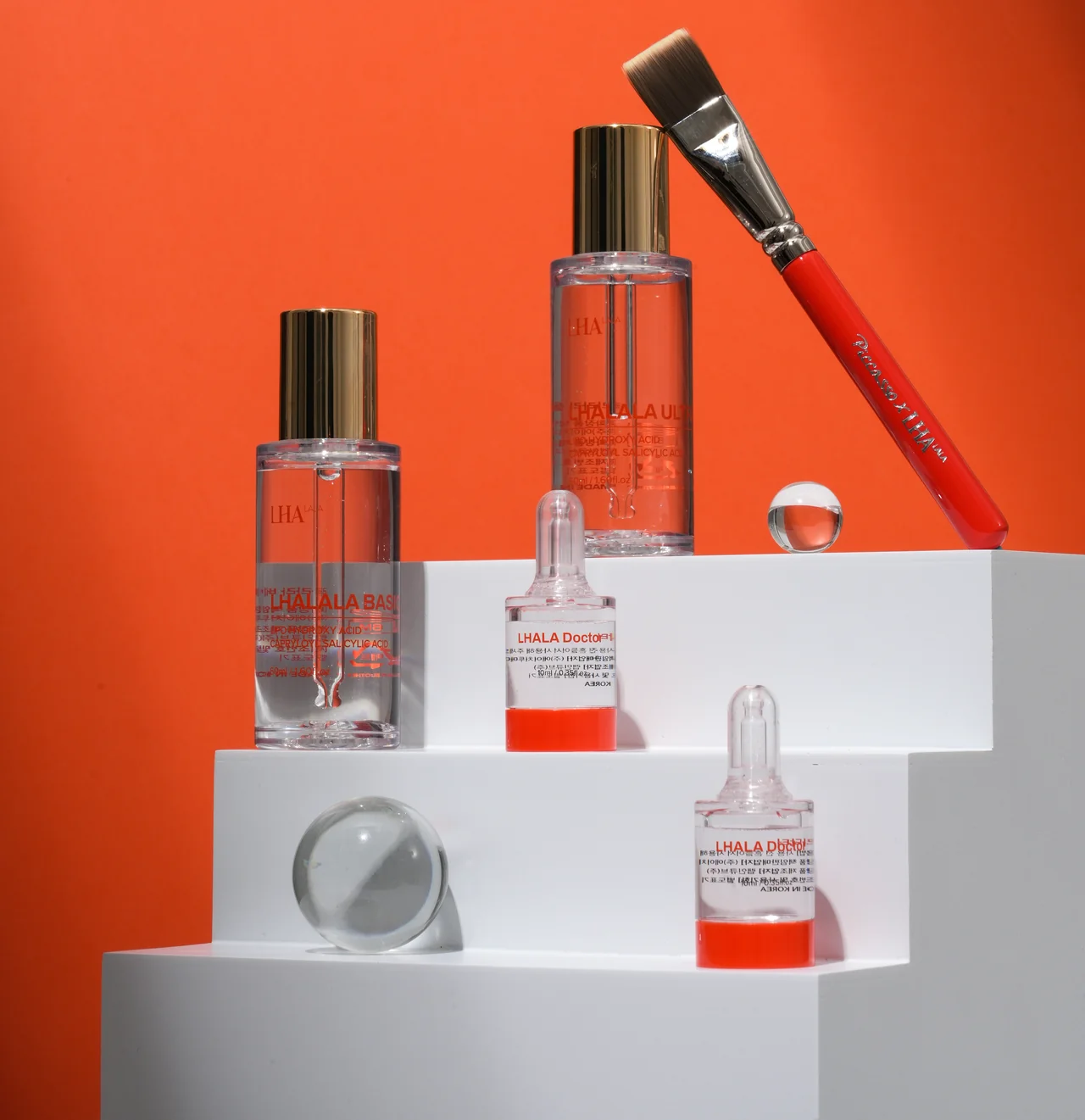 LHALA Peel Basic and Ultra bottles, two LHALA Doctor ampoules and the application brush, on the brand orange